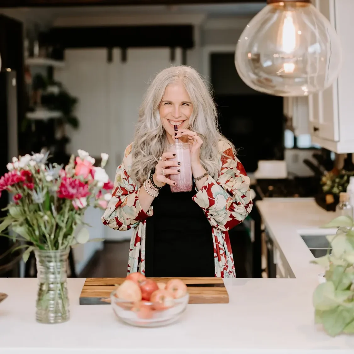 Dawne Sullivan, Holistic Nutritionist, Reiki Master, Cold Immersion Coach, Breathwork Facilitator smiling at camera drinking smoothie