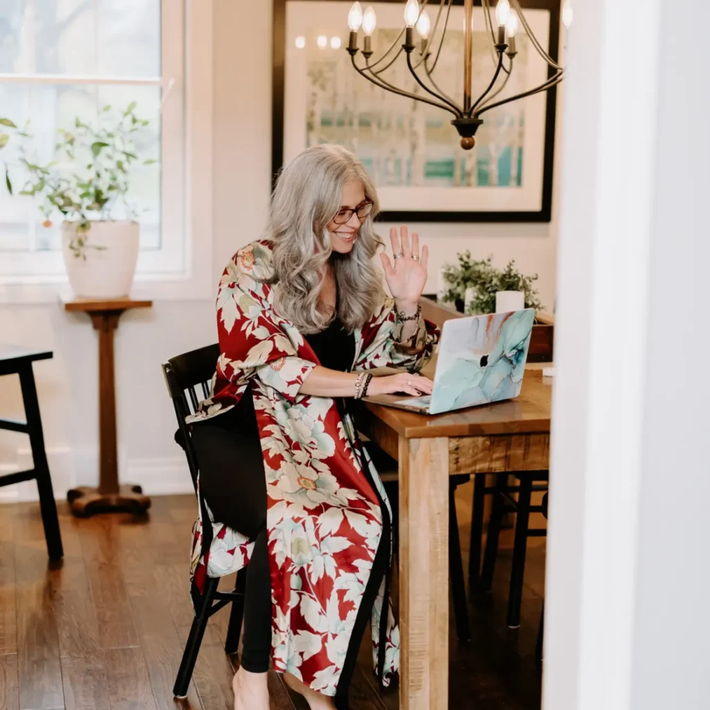 Dawne Sullivan, Holistic Nutritionist, Reiki Master, Cold Immersion Coach, Breathwork Facilitator sitting at kitchen table on laptop smiling