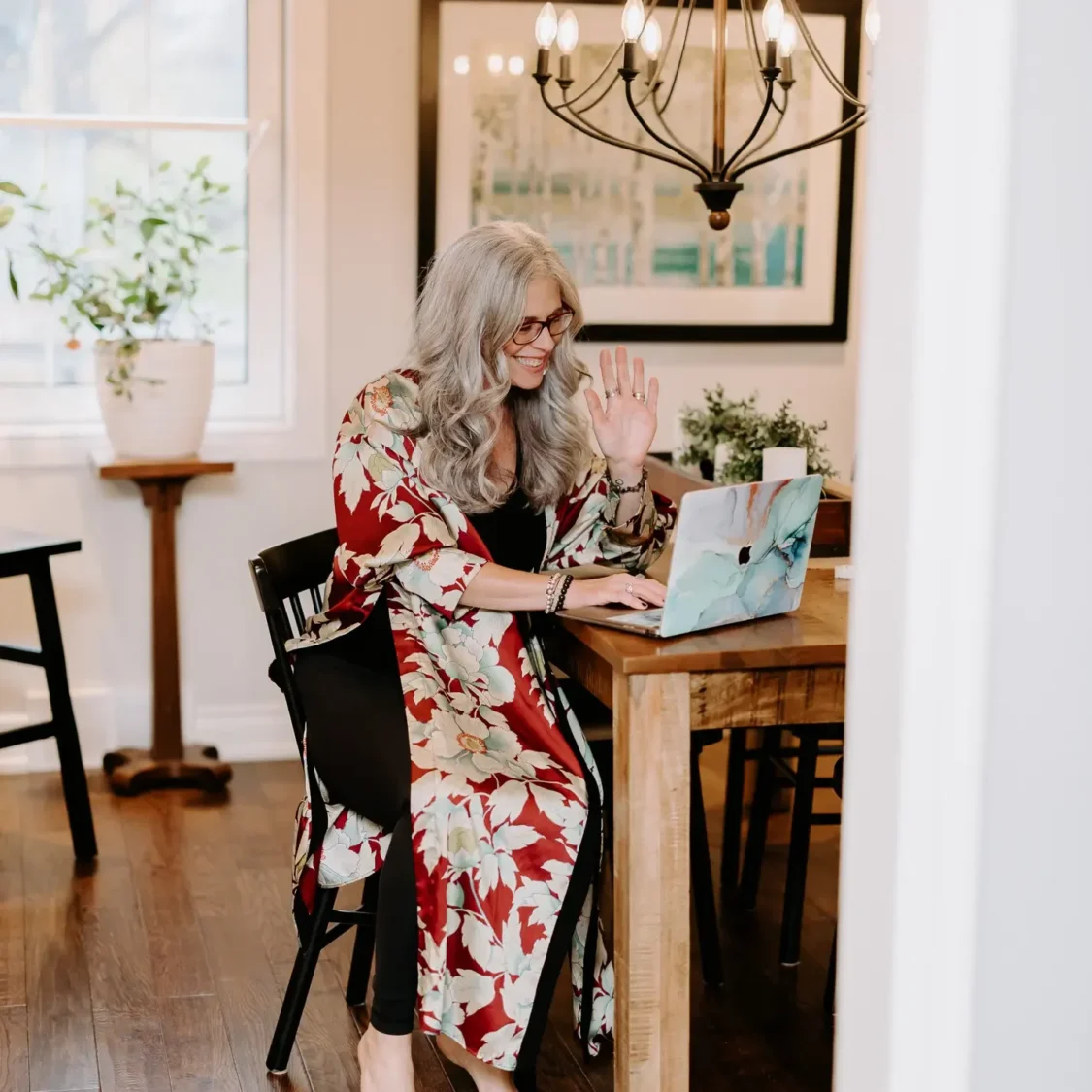 Dawne Sullivan, Holistic Nutritionist, Reiki Master, Cold Immersion Coach, Breathwork Facilitator sitting at kitchen table on laptop smiling
